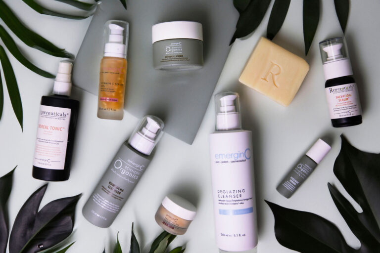 Flat lay of various skincare products surrounded by green tropical leaves on a light background, including cleansers, tonics, and creams.