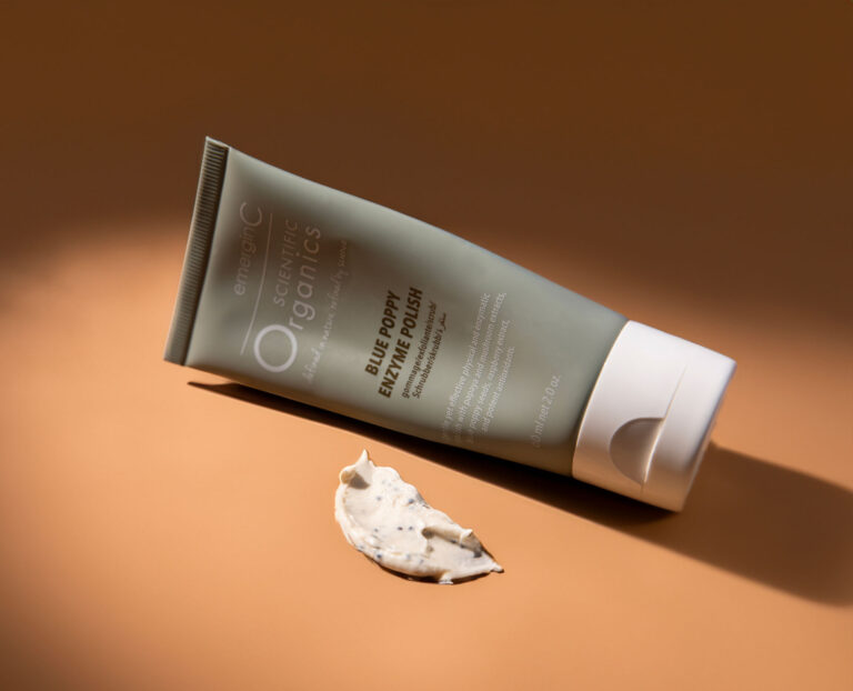 A tube of cosmetic cream lies partially squeezed on a beige surface with a dollop of the cream spilled in front of it under warm lighting. the background and surface are a soft, uniform beige.