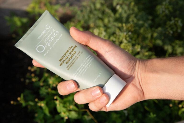 A person holding a tube of botanic organics skincare product with plants in the background.