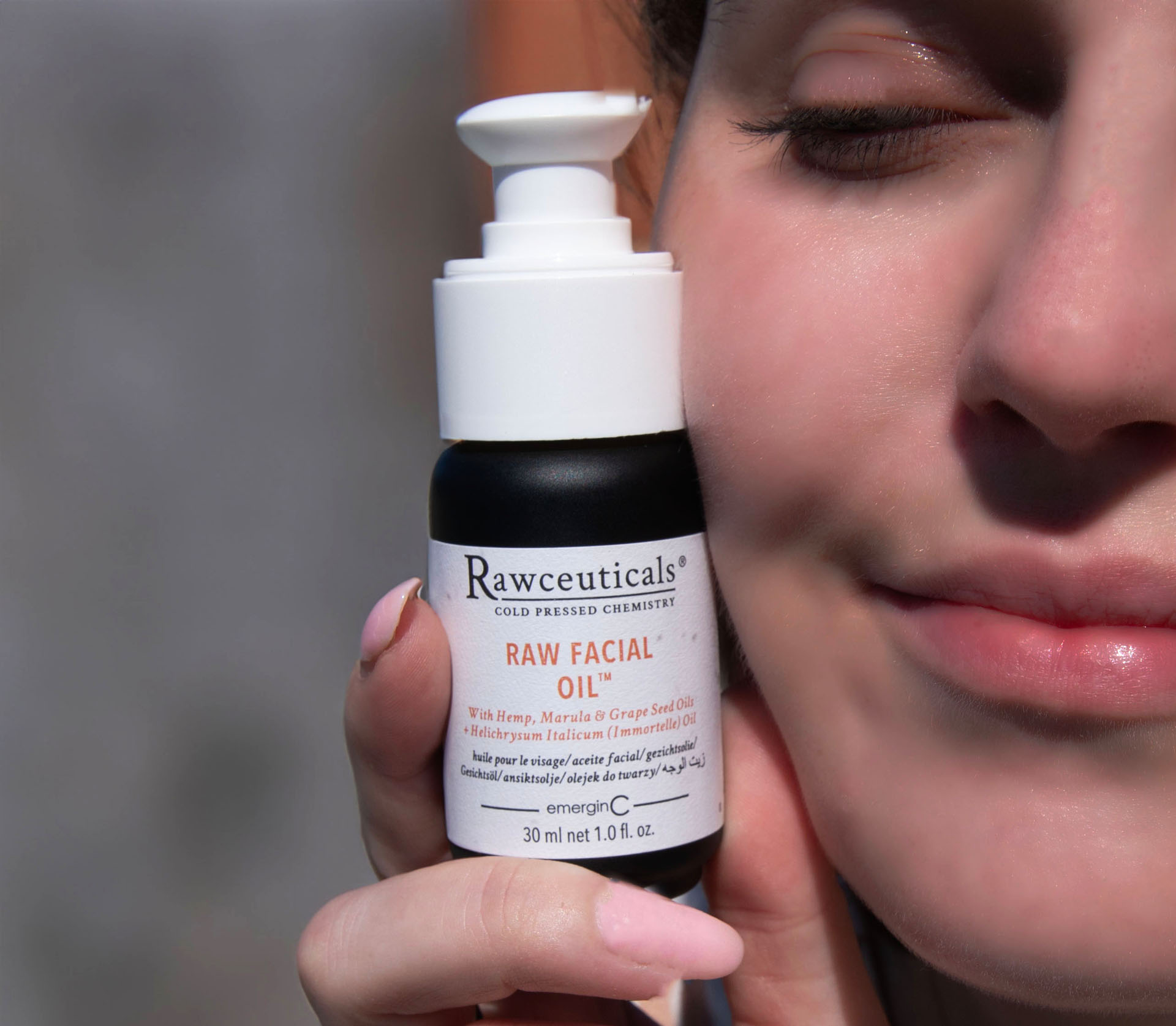 A close-up of a person holding a bottle of rawceuticals facial oil next to their cheek, highlighting the product's natural ingredients for skincare.