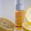 A bottle of emerginc vitamin c serum surrounded by fresh lemon slices, highlighting the citrus ingredient in the skincare product.