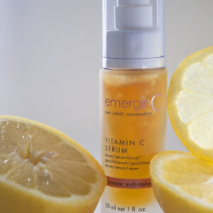 A bottle of emerginc vitamin c serum surrounded by fresh lemon slices, highlighting the citrus ingredient in the skincare product.