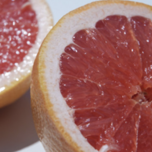 A close-up of a juicy, sliced grapefruit with one half positioned in the foreground, featuring its vibrant pink to red citrus segments.