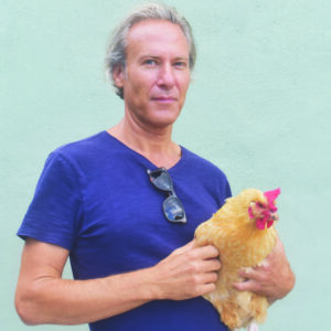 A man in a blue shirt holding a fluffy yellow chicken against a pale green background.