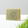 A bar of Scientific Organics Facial Bar with an embossed "so" logo, positioned against a crisp, clean background with a hint of green grass at the bottom right corner, suggesting an eco-friendly and organic product.
