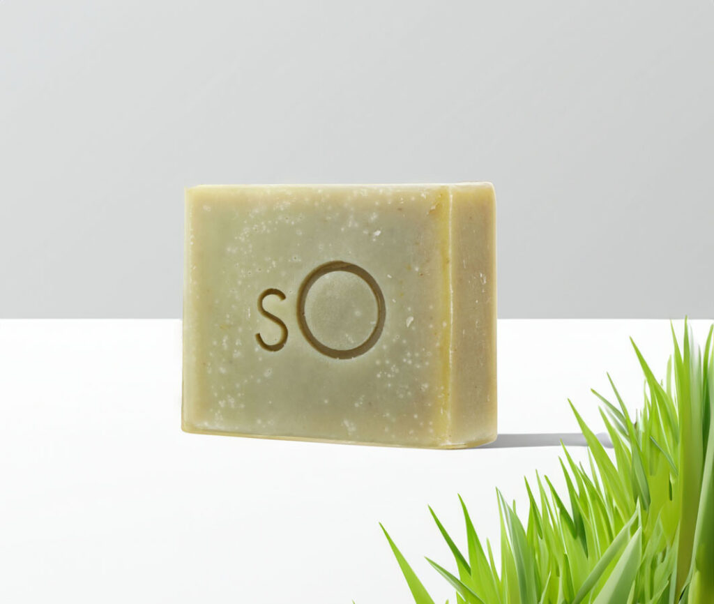 A bar of Scientific Organics Facial Bar with an embossed "so" logo, positioned against a crisp, clean background with a hint of green grass at the bottom right corner, suggesting an eco-friendly and organic product.