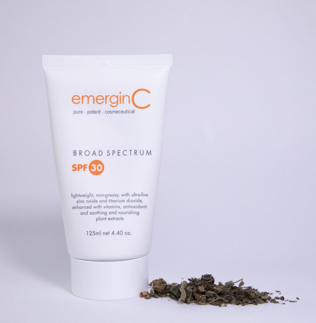 A tube of sun spf 30+ sunscreen displayed against a clean white background with a small pile of loose, dried leaves or botanical ingredients to its side, emphasizing the product's natural components.