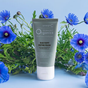 A tube of emerginc scientific organics Blue Poppy Enzyme Polish surrounded by vibrant blue poppy flowers against a calming blue background.
