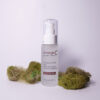 A bottle of emerginc Crease Ease Gel placed on a plain background, flanked by green moss, suggesting a natural skincare theme.