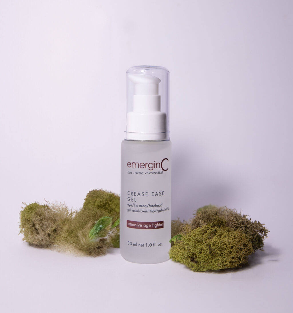 A bottle of emerginc Crease Ease Gel placed on a plain background, flanked by green moss, suggesting a natural skincare theme.