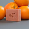 A Signature Facial Bar with an "ec" imprint surrounded by fresh oranges on a grey background, suggesting a citrus-scented cleansing product.
