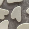 A collection of white, branded Gua Sha massage tools spread out on a gray textured surface.