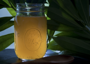 A mason jar filled with golden honey sits beside green leaves with a wooden spoon, embodying nature's sweetness.