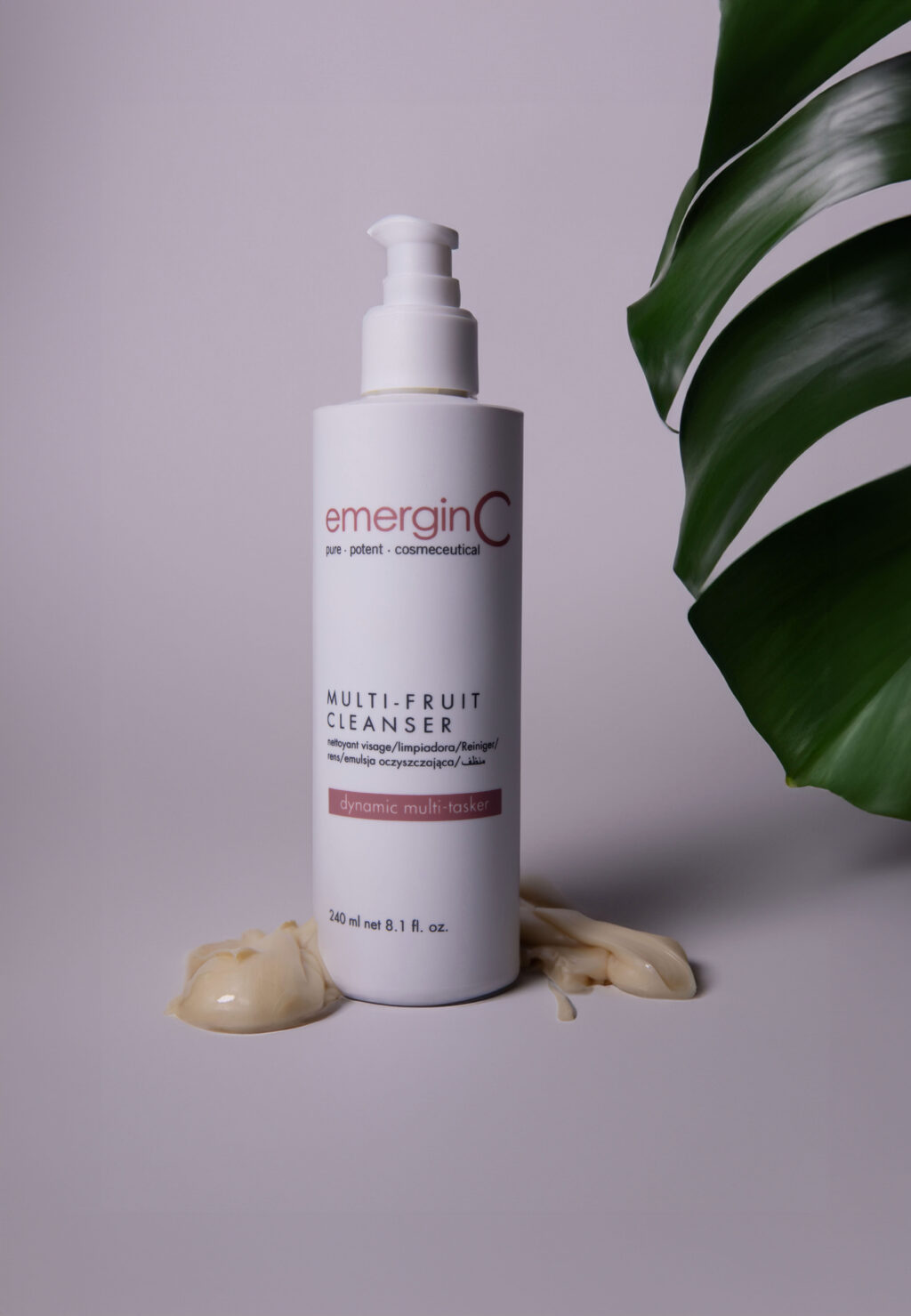 Bottle of emerginc multi-fruit cleanser with a pump dispenser, some multi-fruit cleanser spilled in front and a green leaf in the background, displayed against a neutral background.