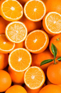 A vivid assembly of fresh oranges, some halved to reveal the juicy, segmented interior, against an orange backdrop.