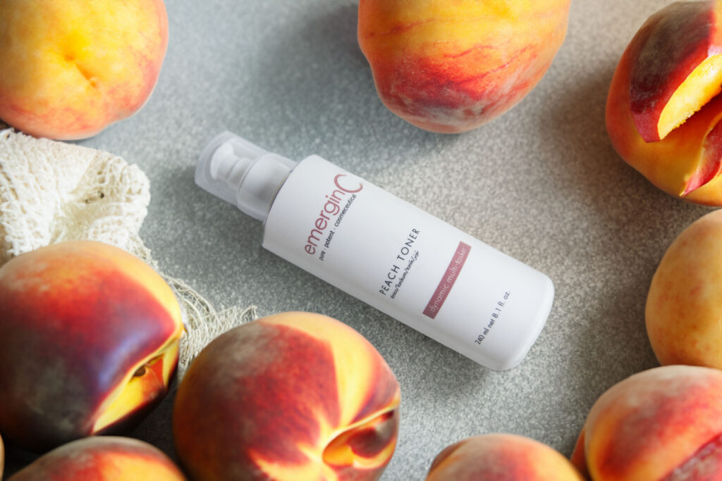 A bottle of peach toner laid out amidst fresh, juicy peaches on a neutral surface, suggesting a natural, fruit-infused skincare routine.