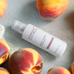 A bottle of peach toner laid out amidst fresh, juicy peaches on a neutral surface, suggesting a natural, fruit-infused skincare routine.