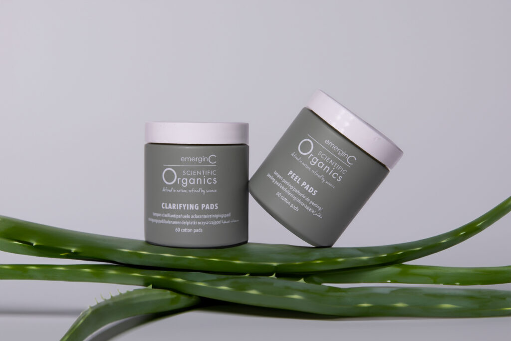 Elegantly presented at-home facial peel + clarifying kit flanked by fresh green aloe vera leaves against a neutral background, emphasizing natural ingredients and purity in cosmetic care.