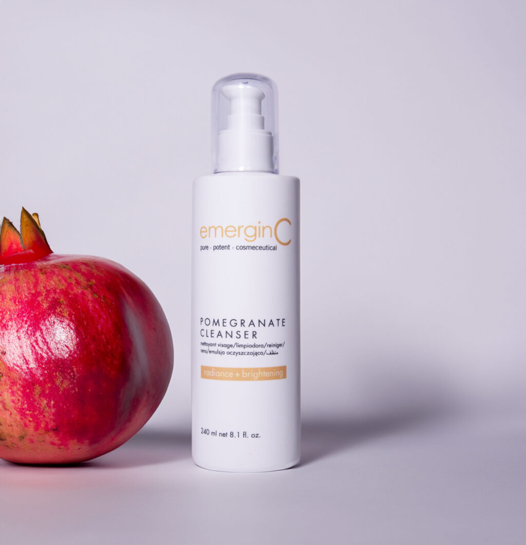 A sleek bottle of pomegranate gel cleanser stands beside a fresh pomegranate, highlighting the product's key ingredient for a radiant and brightening skin care routine.