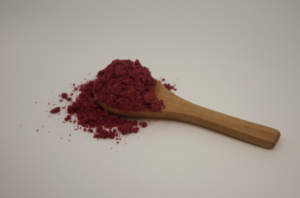 A wooden spoon overflowing with vibrant red powder on a neutral background.