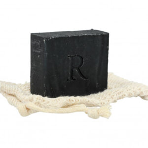 A Rawceuticals Facial Bar with the letter "r" embossed on it, resting on a cream-colored woven cloth against a white background.