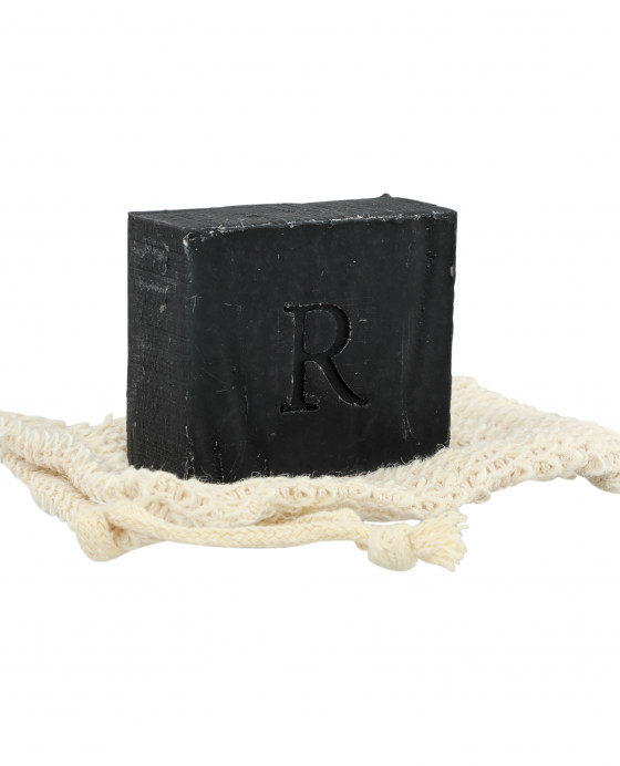 A Rawceuticals Facial Bar with the letter "r" embossed on it, resting on a cream-colored woven cloth against a white background.