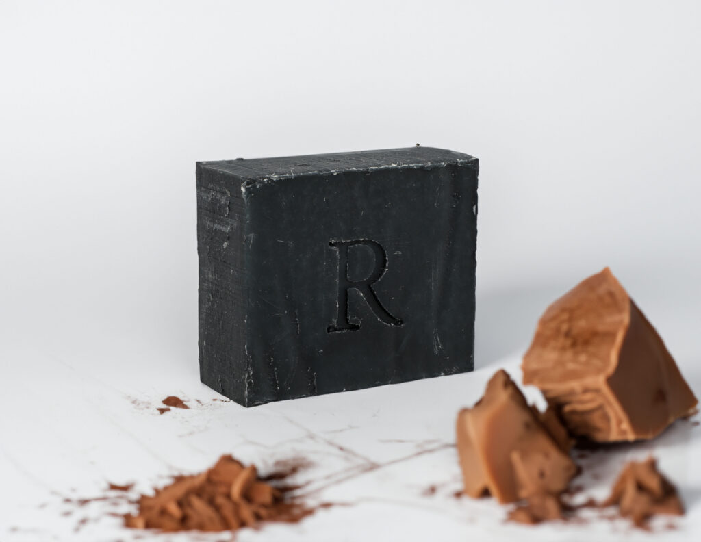 A Rawceuticals Facial Bar with the letter 'r' embossed on it, surrounded by shavings and chunks of a similar substance.