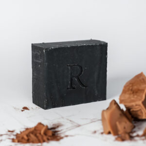 A Rawceuticals Facial Bar with the letter 'r' embossed on it, surrounded by shavings and chunks of a similar substance.