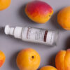 Bottle of swift lift® peptide firming serum surrounded by fresh peaches on a gray surface.