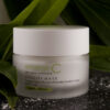 A jar of emerginc vitality mask positioned amongst lush green leaves with a sprinkle of white granules on the surface below, conveying a sense of natural skincare.