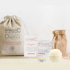 A serene spa-like display featuring the At-Home Luxury Spa Kit - Signature, a rawceuticals cleanser, and a bath bomb, all arranged thoughtfully on a neutral background with soft lighting, suggesting organic and luxurious self-care.