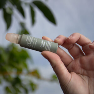 A hand holding a small tube of eyelight serum with a blurred natural background, suggesting a connection to nature and organic ingredients.