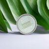 A container of emerginc scientific organics in lips we trust super antioxidant lip balm against a backdrop of lush green leaves.