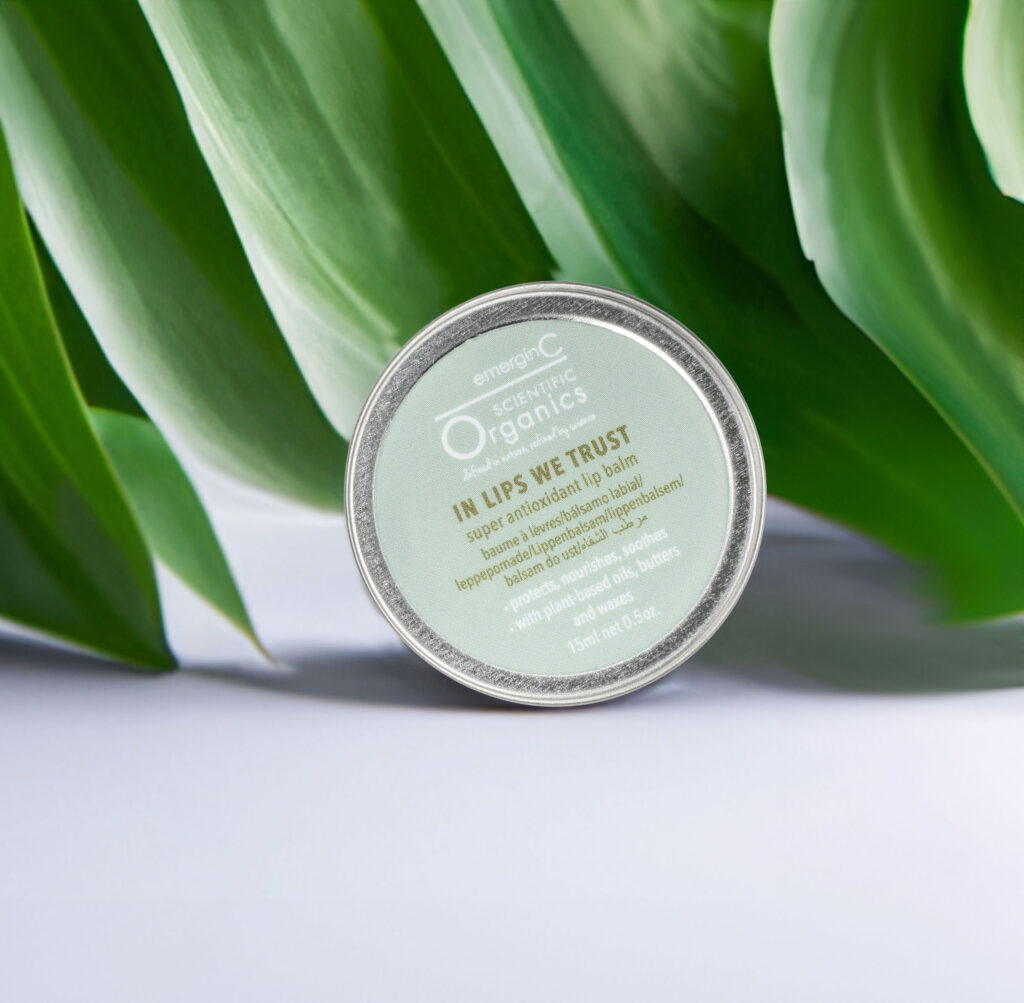 A container of emerginc scientific organics in lips we trust super antioxidant lip balm against a backdrop of lush green leaves.