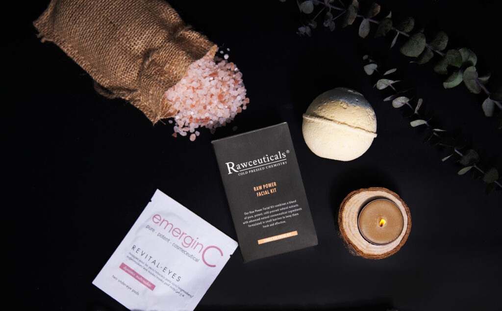 A tranquil and sophisticated At-Home Luxury Spa Kit - Rawceuticals concept with a focus on natural wellness, featuring an assortment of boutique skincare products, himalayan pink salt, a lit candle, and calming botanical accents on a sleek, dark background.