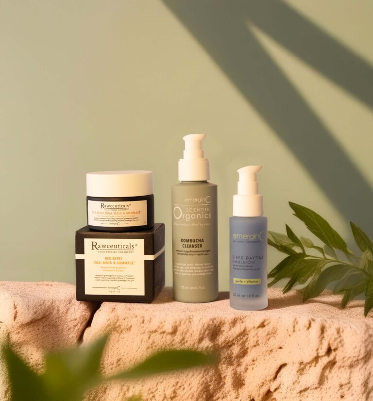 Four skincare products, including jars and pump bottles, are arranged on a sandy surface with green leaves in the corner. Soft natural sunlight casts shadows, creating a soothing and organic atmosphere perfect for premium skin care lines for spas.