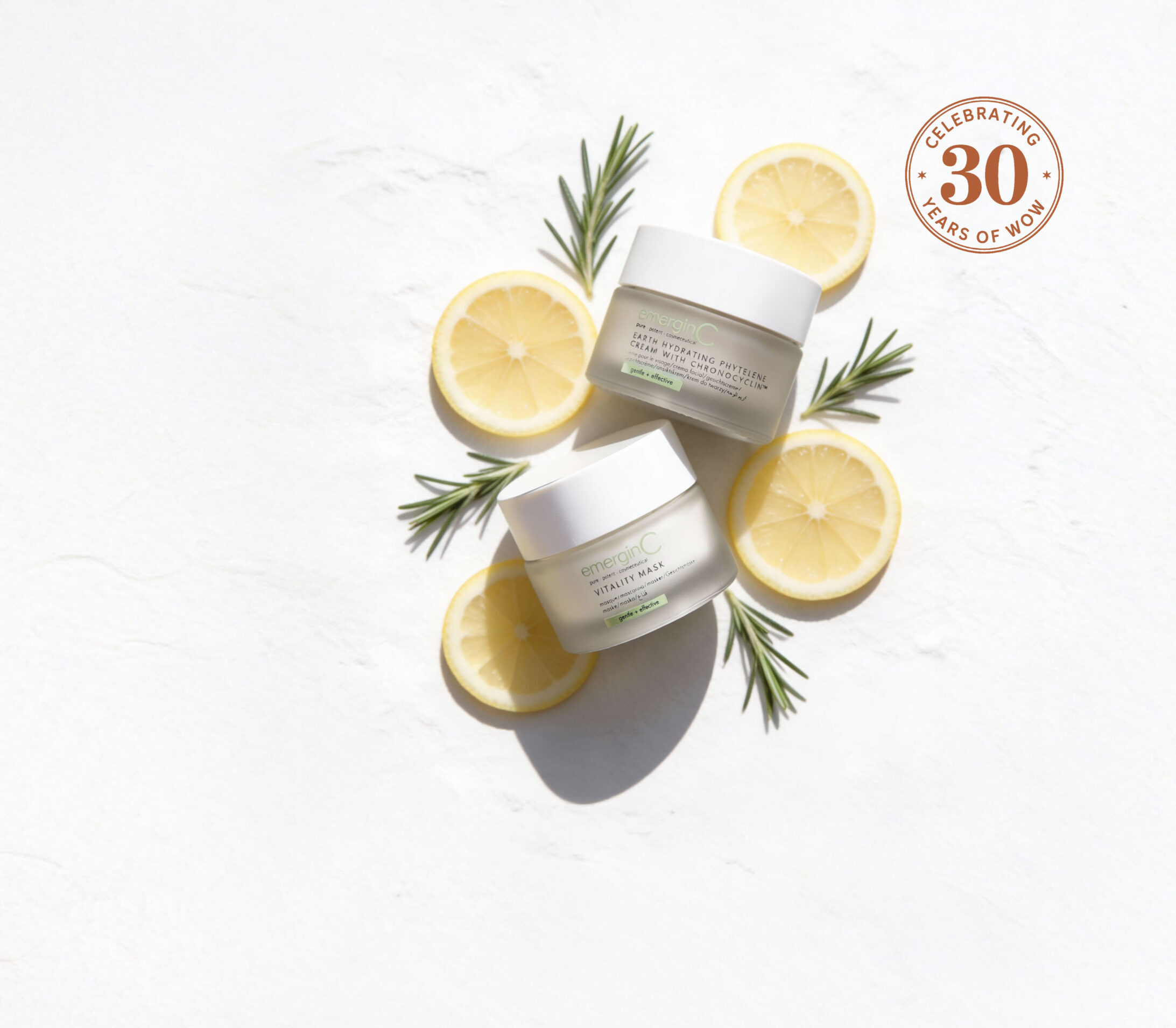 Three professional luxury skin care cream jars are arranged on a white surface with lemon slices and rosemary sprigs. A circular badge in the top right corner reads 