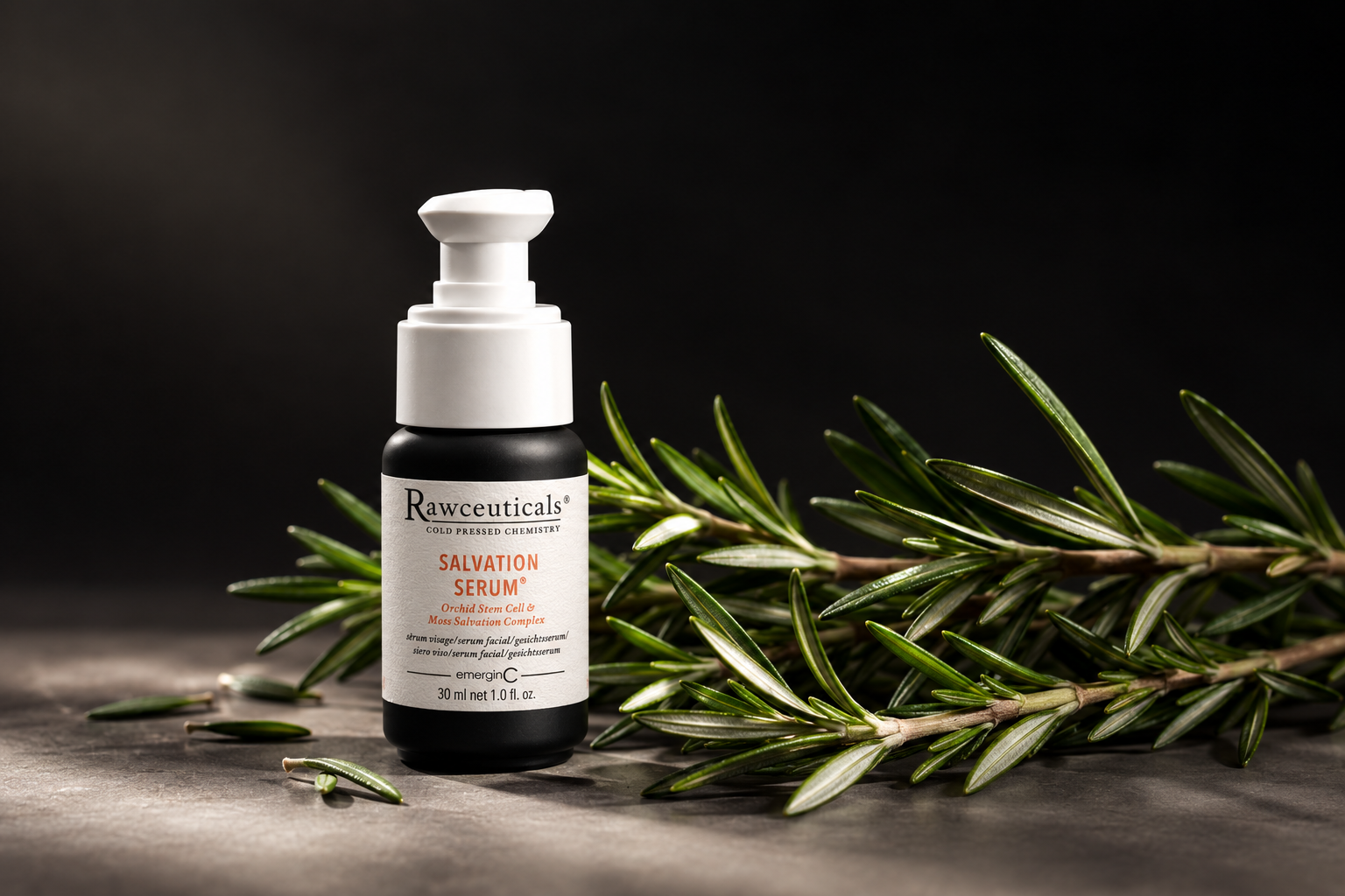 A bottle of Rawceuticals Salvation Serum stands upright next to fresh rosemary sprigs on a dark surface, embodying professional luxury skin care with a softly lit background.